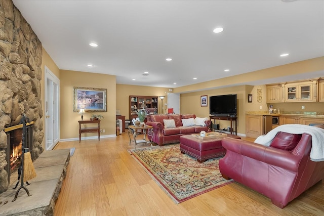 living room with light hardwood / wood-style floors, a stone fireplace, and indoor bar