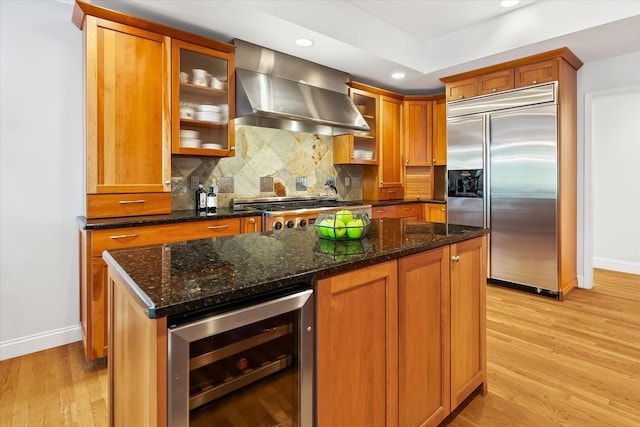 kitchen featuring stainless steel appliances, wall chimney range hood, wine cooler, light hardwood / wood-style floors, and a kitchen island