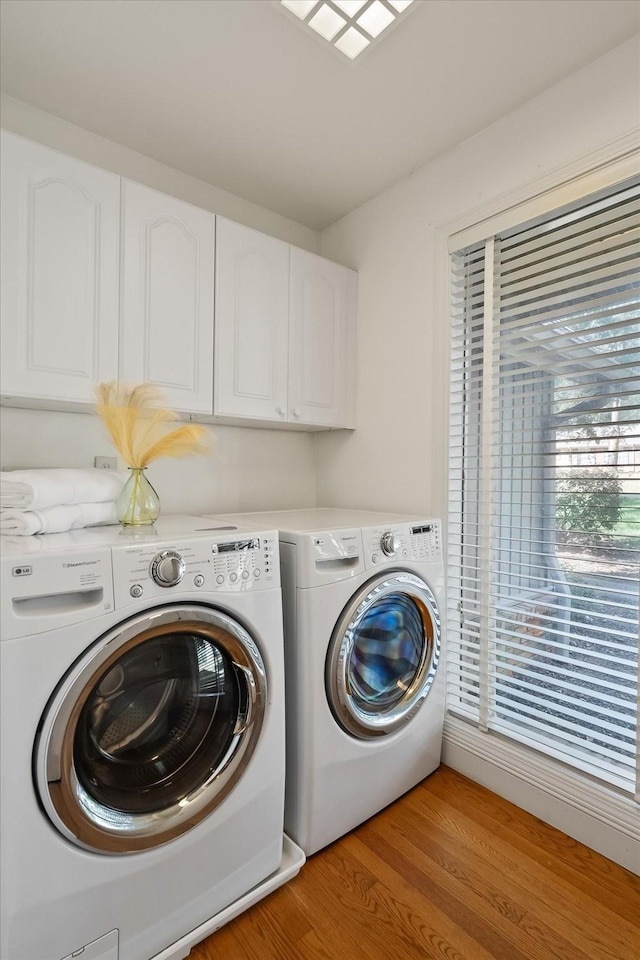 washroom with cabinets, washing machine and clothes dryer, and light hardwood / wood-style flooring