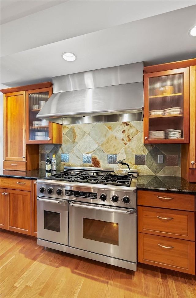 kitchen with tasteful backsplash, light hardwood / wood-style floors, wall chimney exhaust hood, dark stone countertops, and stainless steel stove