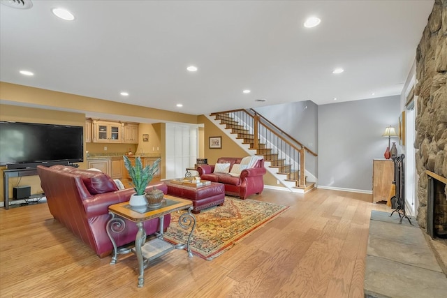 living room featuring light hardwood / wood-style floors, a stone fireplace, and bar