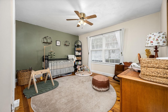 bedroom with wood-type flooring, a nursery area, and ceiling fan