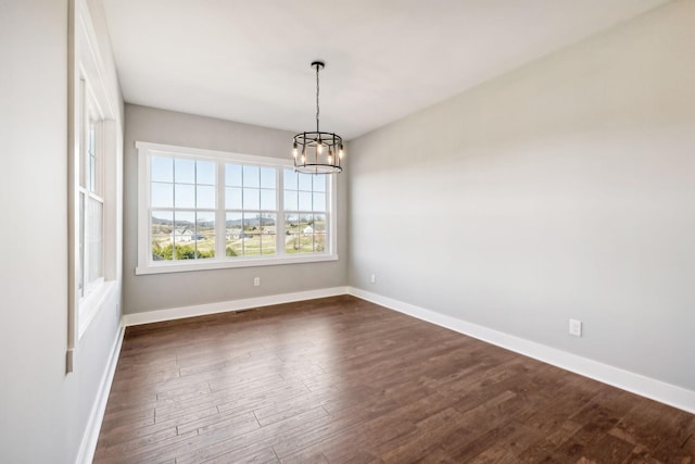 spare room with dark wood-type flooring and an inviting chandelier