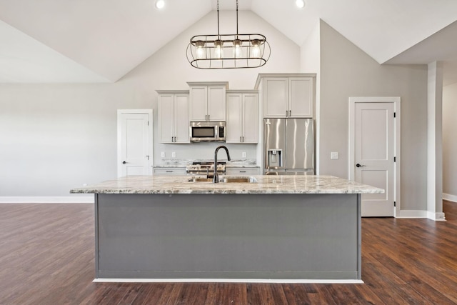 kitchen featuring a center island with sink, sink, appliances with stainless steel finishes, dark hardwood / wood-style flooring, and light stone counters