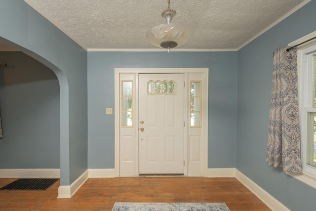 entrance foyer featuring a textured ceiling, a healthy amount of sunlight, wood-type flooring, and crown molding