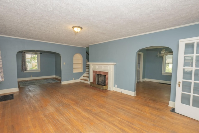 unfurnished living room with hardwood / wood-style flooring, crown molding, a fireplace, and an inviting chandelier