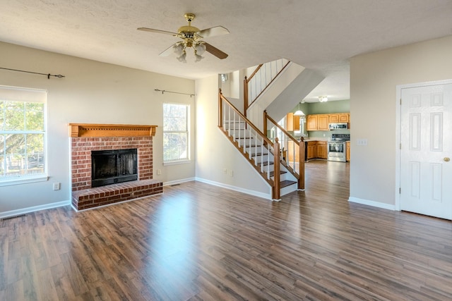 unfurnished living room featuring ceiling fan, a fireplace, dark wood-type flooring, and a textured ceiling