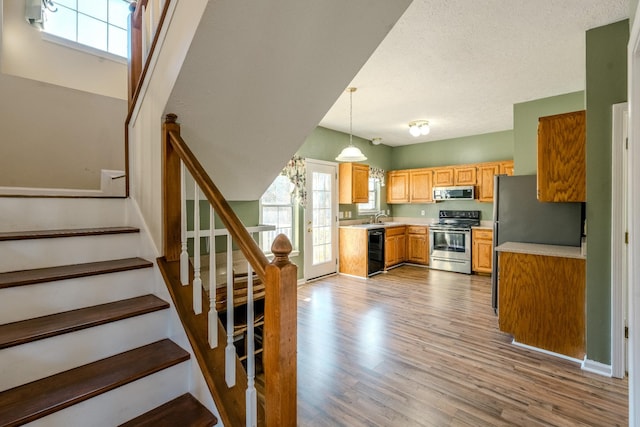 kitchen with sink, light wood-type flooring, a textured ceiling, decorative light fixtures, and stainless steel appliances