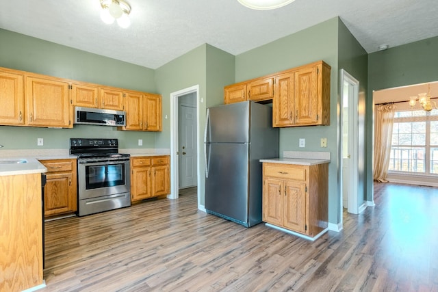 kitchen with sink, a textured ceiling, appliances with stainless steel finishes, light hardwood / wood-style floors, and a chandelier