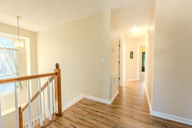 hall with hardwood / wood-style floors, a textured ceiling, and a notable chandelier