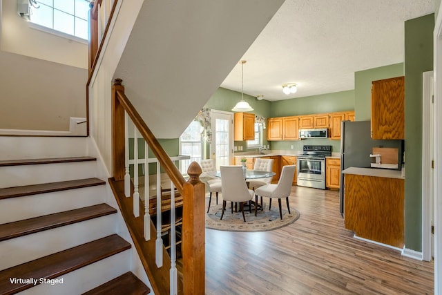 interior space with a textured ceiling, stainless steel appliances, sink, light hardwood / wood-style floors, and hanging light fixtures