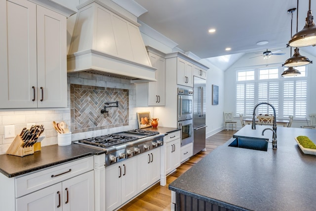 kitchen featuring sink, light hardwood / wood-style flooring, premium range hood, pendant lighting, and appliances with stainless steel finishes