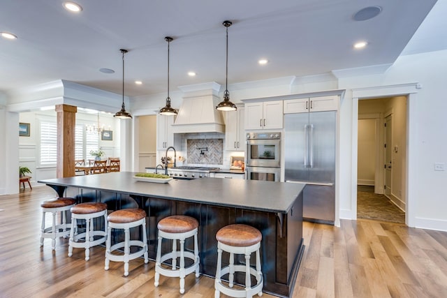 kitchen featuring custom exhaust hood, light hardwood / wood-style floors, stainless steel appliances, and decorative light fixtures