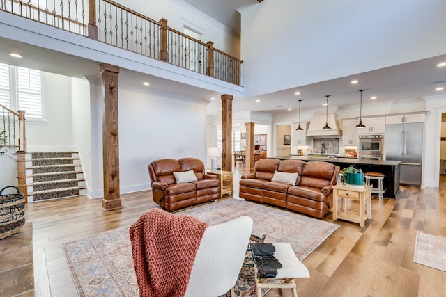 living room featuring light wood-type flooring, a towering ceiling, decorative columns, and sink