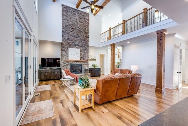 living room featuring a stone fireplace, ceiling fan, light wood-type flooring, a towering ceiling, and decorative columns