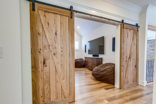 hallway with hardwood / wood-style flooring, a barn door, ornamental molding, and vaulted ceiling