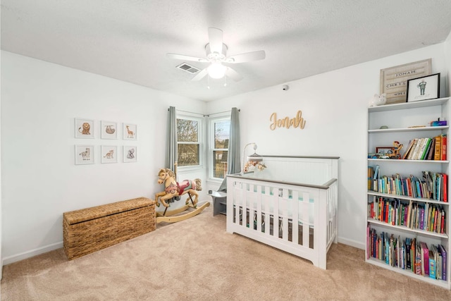 carpeted bedroom with ceiling fan, a nursery area, and a textured ceiling