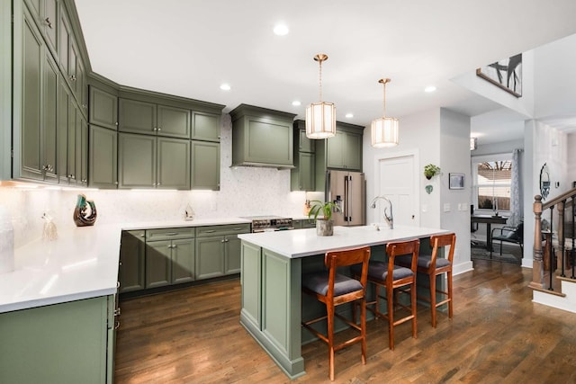 kitchen featuring stainless steel appliances, dark hardwood / wood-style floors, pendant lighting, a center island with sink, and green cabinetry