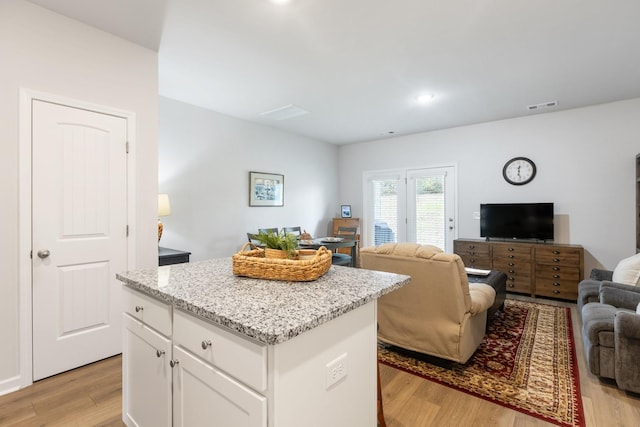 kitchen with white cabinets, a kitchen island, light stone countertops, and light hardwood / wood-style flooring