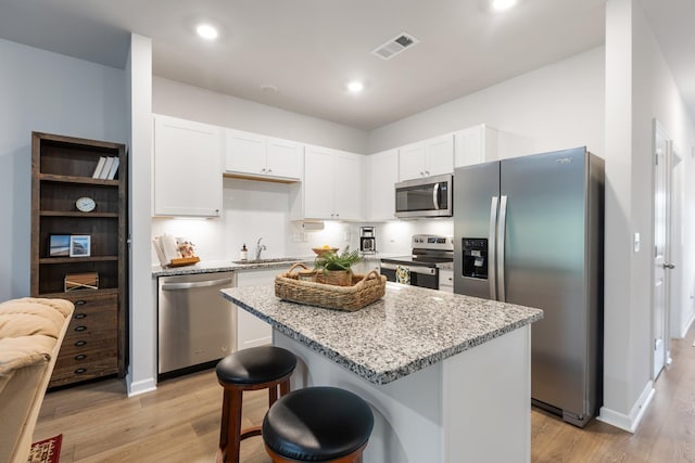 kitchen with appliances with stainless steel finishes, light wood-type flooring, sink, a center island, and white cabinetry