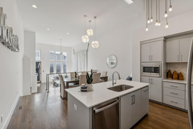 kitchen with sink, dark hardwood / wood-style floors, pendant lighting, a kitchen island with sink, and appliances with stainless steel finishes