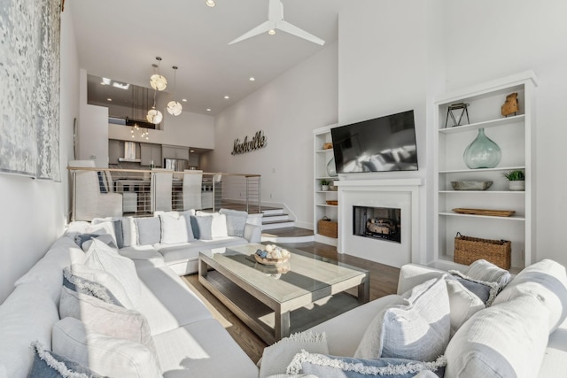 living room with ceiling fan, built in features, wood-type flooring, and a high ceiling