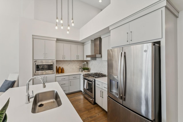 kitchen featuring appliances with stainless steel finishes, wall chimney exhaust hood, dark wood-type flooring, sink, and hanging light fixtures