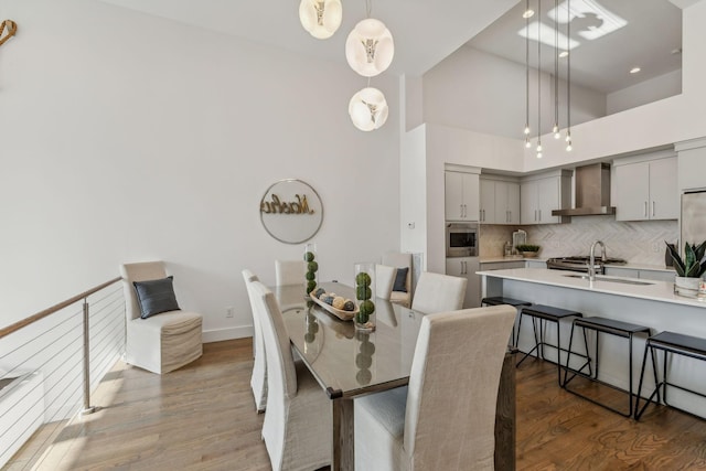 dining area featuring sink, wood-type flooring, and a high ceiling