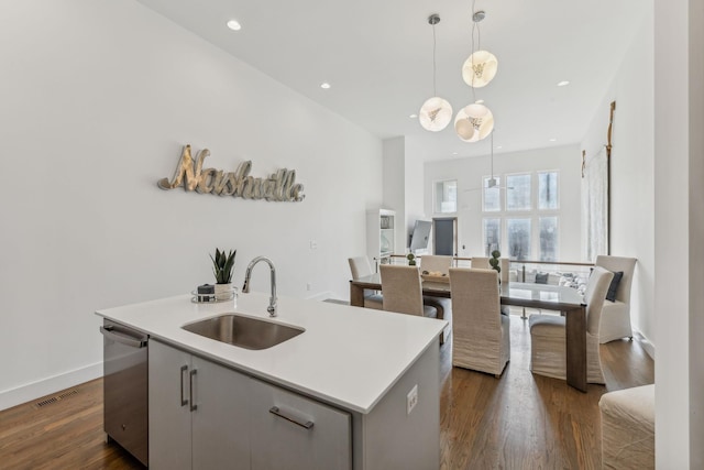 kitchen featuring dishwasher, sink, dark wood-type flooring, pendant lighting, and a center island with sink