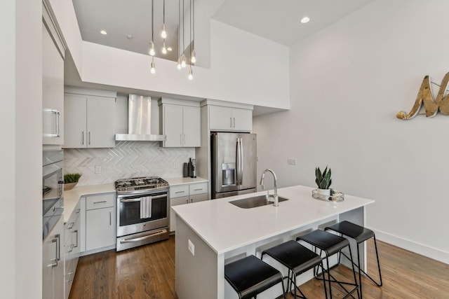 kitchen featuring a center island with sink, hardwood / wood-style flooring, wall chimney range hood, and appliances with stainless steel finishes