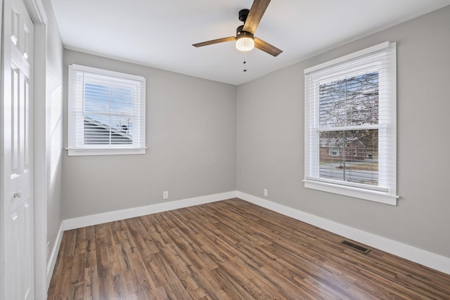 empty room with plenty of natural light, ceiling fan, and dark wood-type flooring