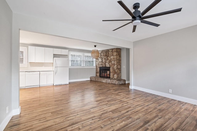 unfurnished living room with a stone fireplace, ceiling fan, and light wood-type flooring