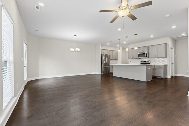 kitchen featuring decorative light fixtures, gray cabinets, decorative backsplash, a center island with sink, and appliances with stainless steel finishes