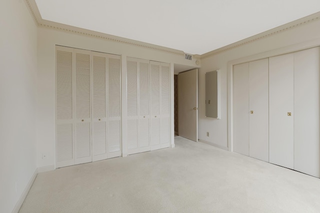 unfurnished bedroom with multiple closets, light carpet, and crown molding