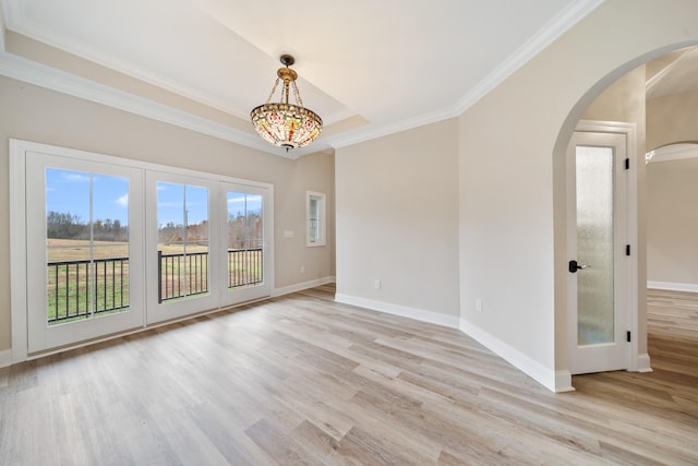 empty room with a tray ceiling, ornamental molding, and light wood-type flooring