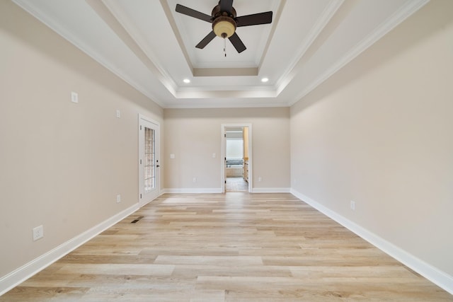 empty room with ceiling fan, a raised ceiling, light wood-type flooring, and crown molding