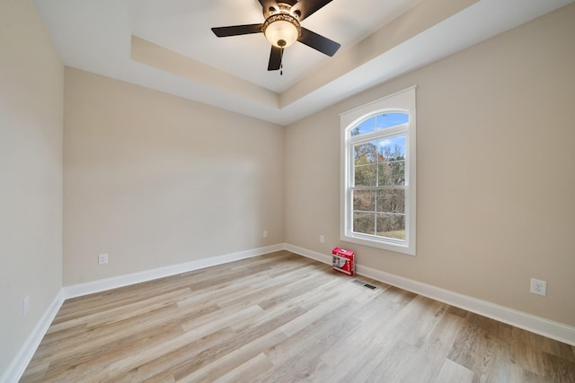 spare room featuring light wood-type flooring, a tray ceiling, and ceiling fan