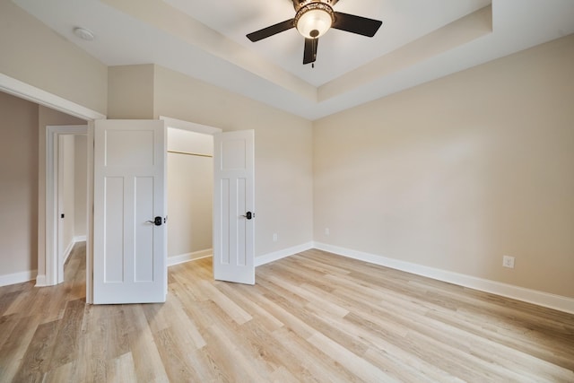 unfurnished bedroom featuring light wood-type flooring, a raised ceiling, and ceiling fan