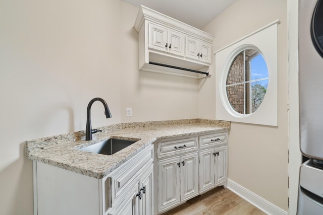 kitchen with white cabinets, light stone countertops, light wood-type flooring, and sink