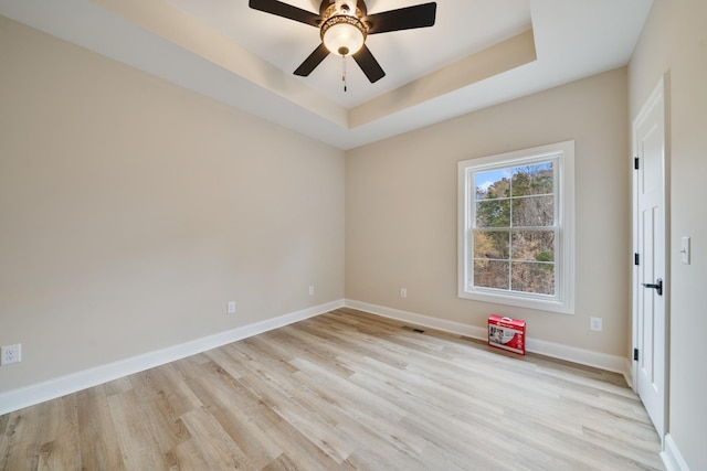 empty room with a raised ceiling, ceiling fan, and light wood-type flooring