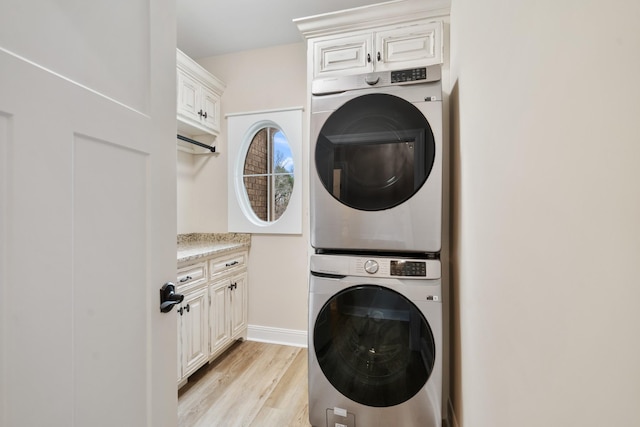 laundry area with stacked washer / drying machine, cabinets, and light wood-type flooring