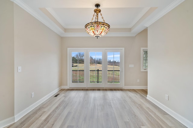 unfurnished dining area with a tray ceiling, crown molding, and light hardwood / wood-style floors