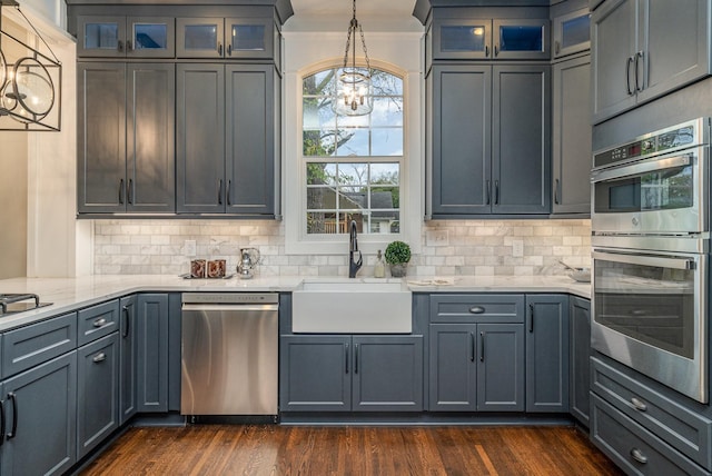 kitchen featuring decorative backsplash, appliances with stainless steel finishes, dark wood-type flooring, sink, and hanging light fixtures