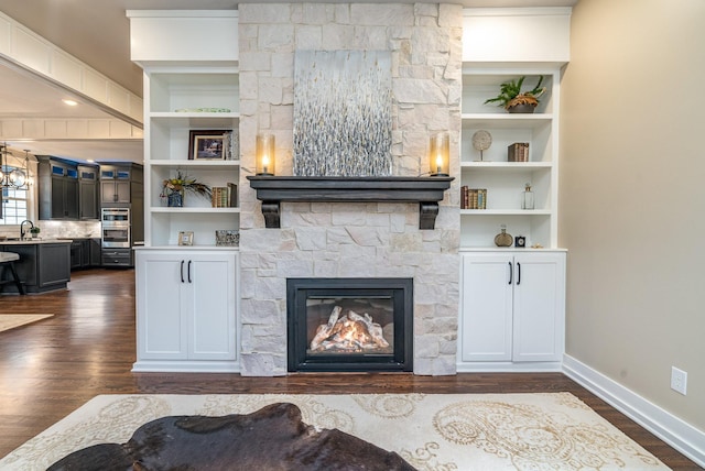 living room featuring a fireplace, built in features, sink, and dark wood-type flooring