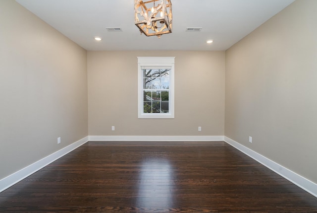 spare room featuring dark hardwood / wood-style flooring and an inviting chandelier