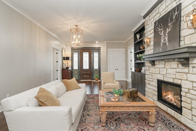 living room featuring crown molding, built in shelves, a fireplace, a notable chandelier, and wood-type flooring