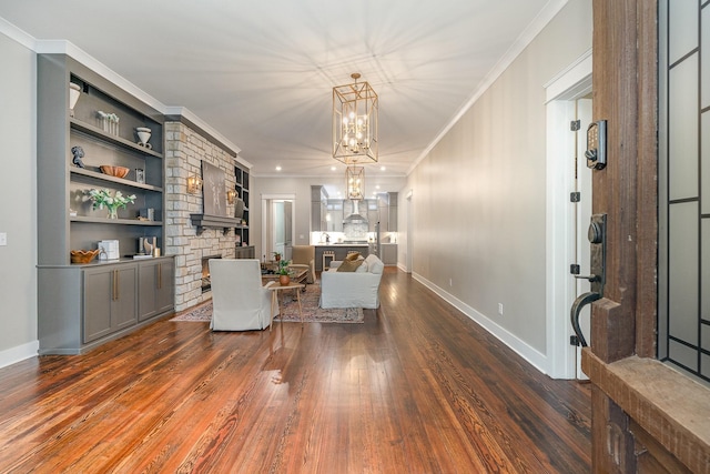 living room with a stone fireplace, crown molding, dark hardwood / wood-style floors, built in shelves, and a notable chandelier