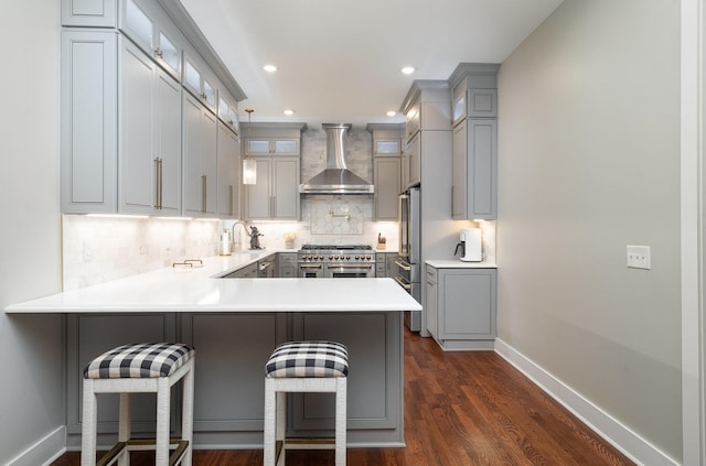 kitchen with kitchen peninsula, dark wood-type flooring, wall chimney range hood, range with two ovens, and a breakfast bar area