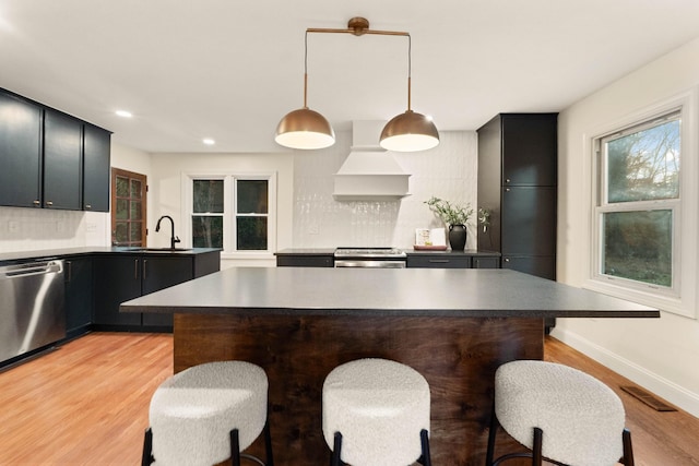 kitchen featuring appliances with stainless steel finishes, tasteful backsplash, custom range hood, sink, and hanging light fixtures