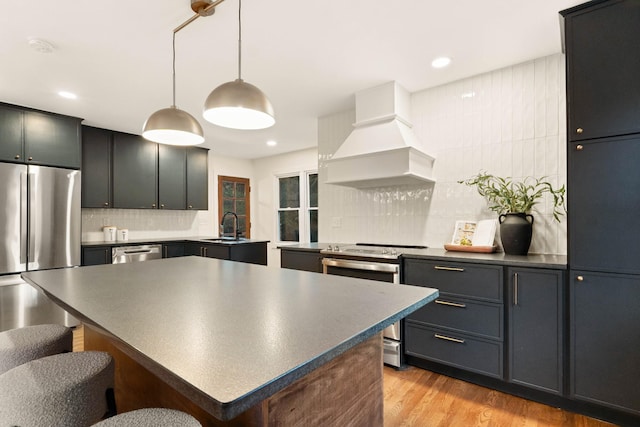 kitchen with custom exhaust hood, sink, hanging light fixtures, light wood-type flooring, and stainless steel appliances